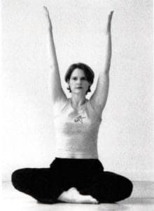 Cyndi Lee sitting with her arms raised over her head.