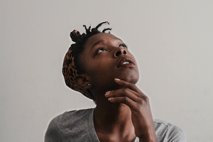 A girl thinking and looking upward. She has a leopard printed scarf tied around her hair and is wearing a grey shirt.