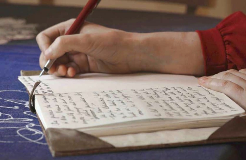 A hand writes on a journal with a pen.