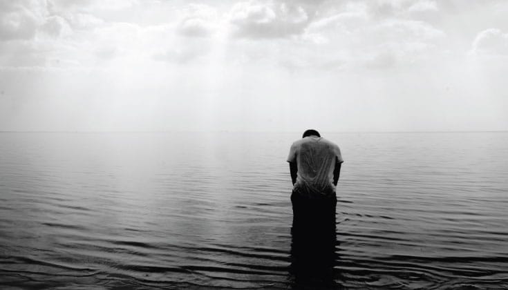 Person standing in the ocean. The water is calm and the photo is in black and white.