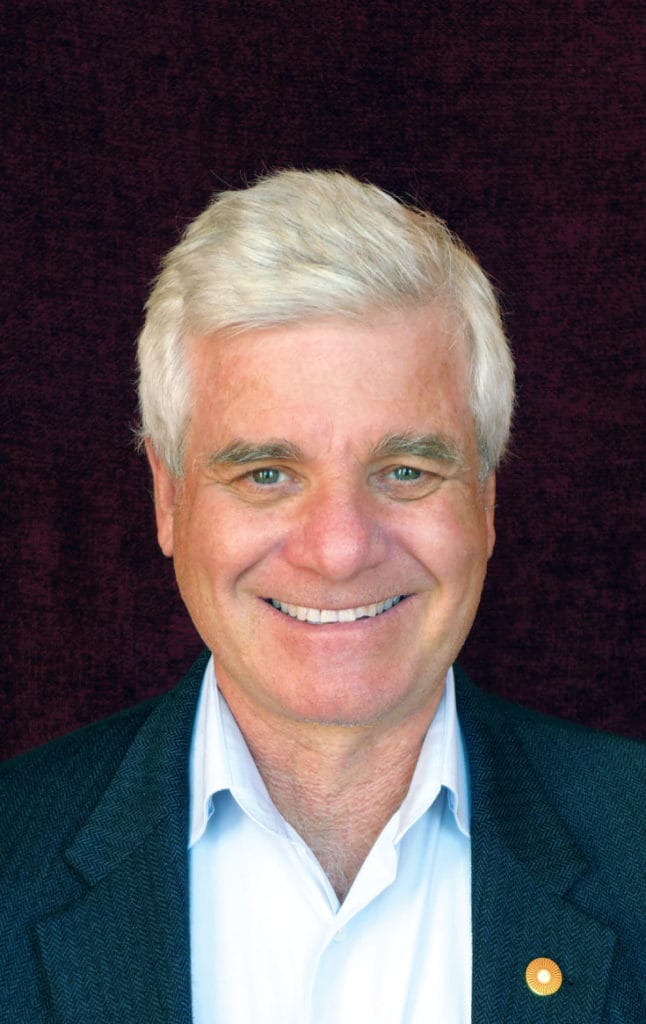 Portrait of a man smiling. He is wearing a dress shirt under a suit coat.
