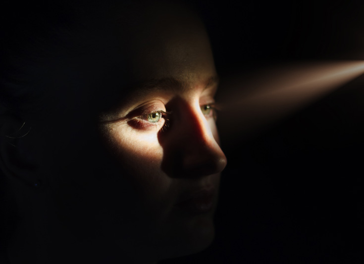 A woman in shadow with the light peeking over her eyes.