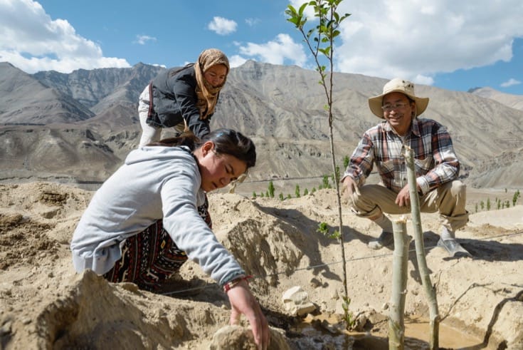 Sonam Wangchuk and two student crouched around a sapling.