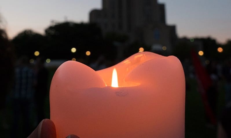 A pink lit candle being held up against a city background.