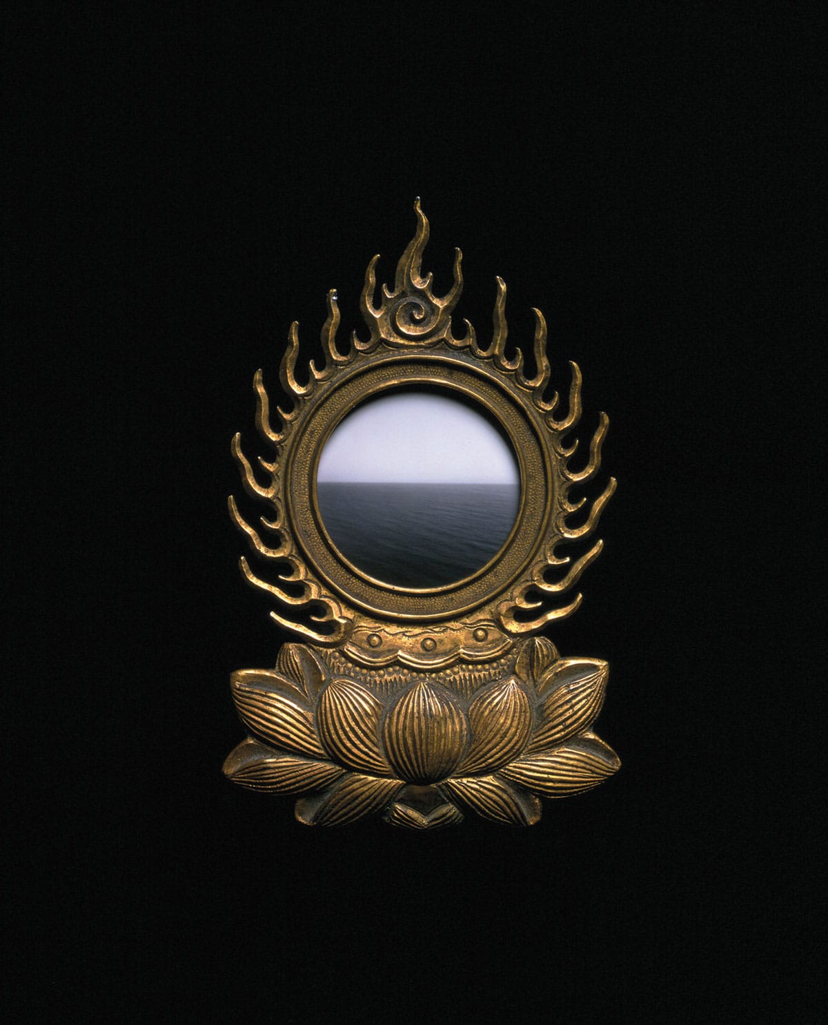 A brass mirror reflecting the ocean against a black wall.