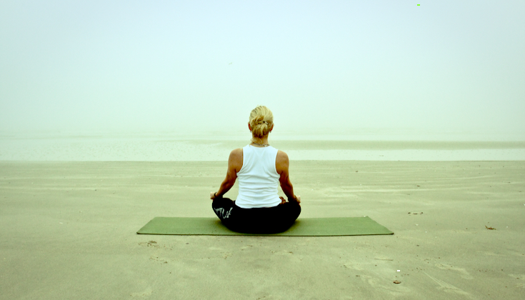 Woman meditating on a foggy beach.