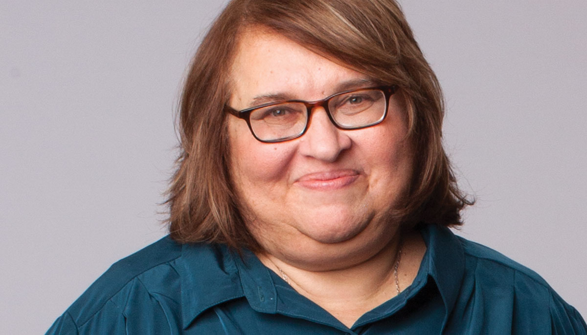 Sharon Salzberg. She is smiling and wearing a teal button up shirt.