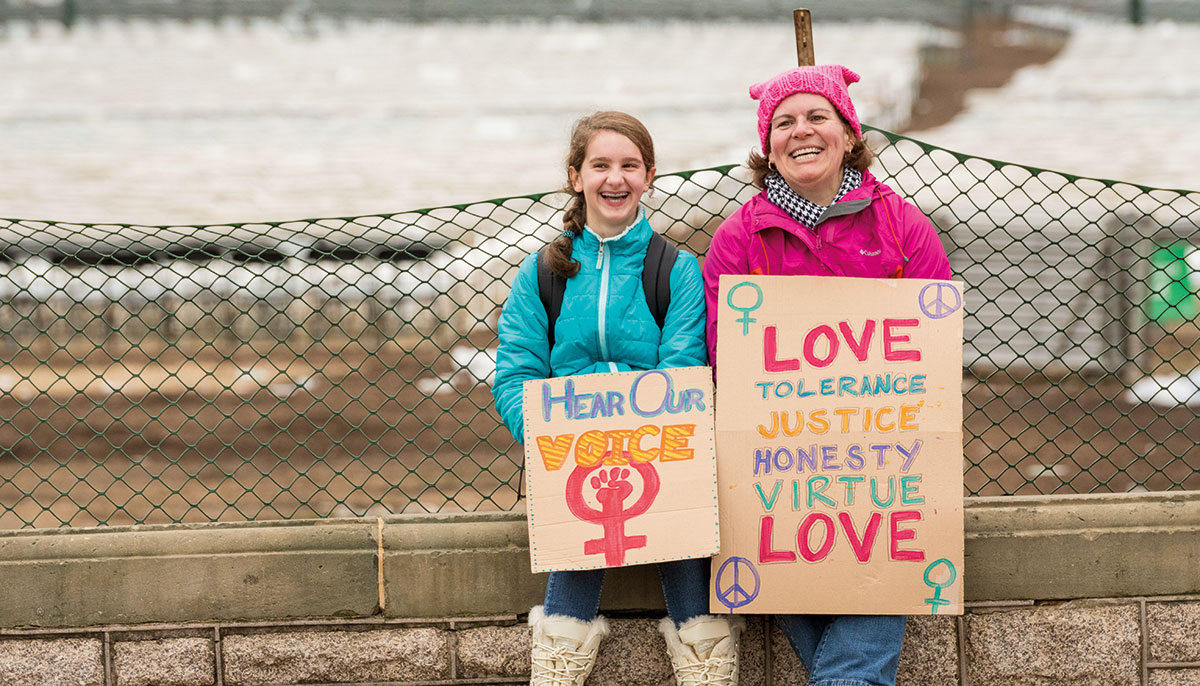A mother and daughter at the Women's March in Washington in 2017, holding signs that say 'Hear our voice" and "love, tolerance, justice, honesty, virtue, love"