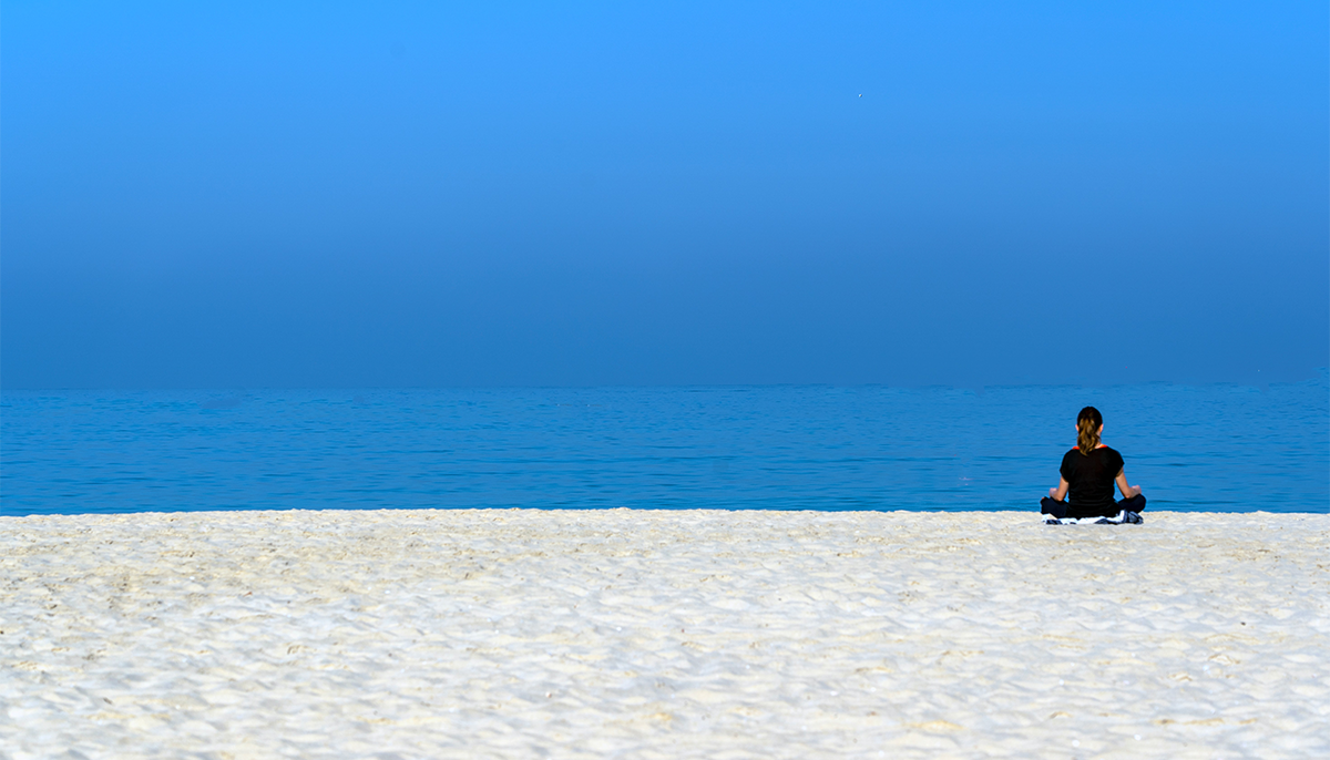 Woman meditating on beach.