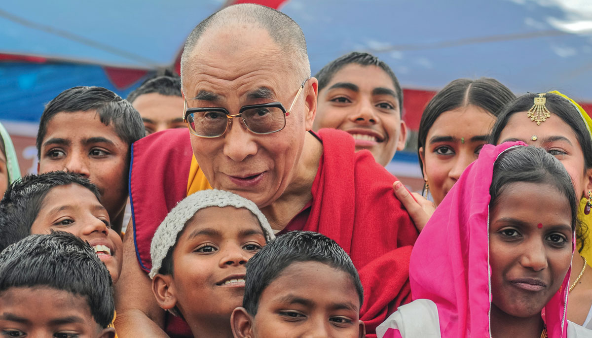 The Dalai Lama with a crowd of children. They are all smiling.