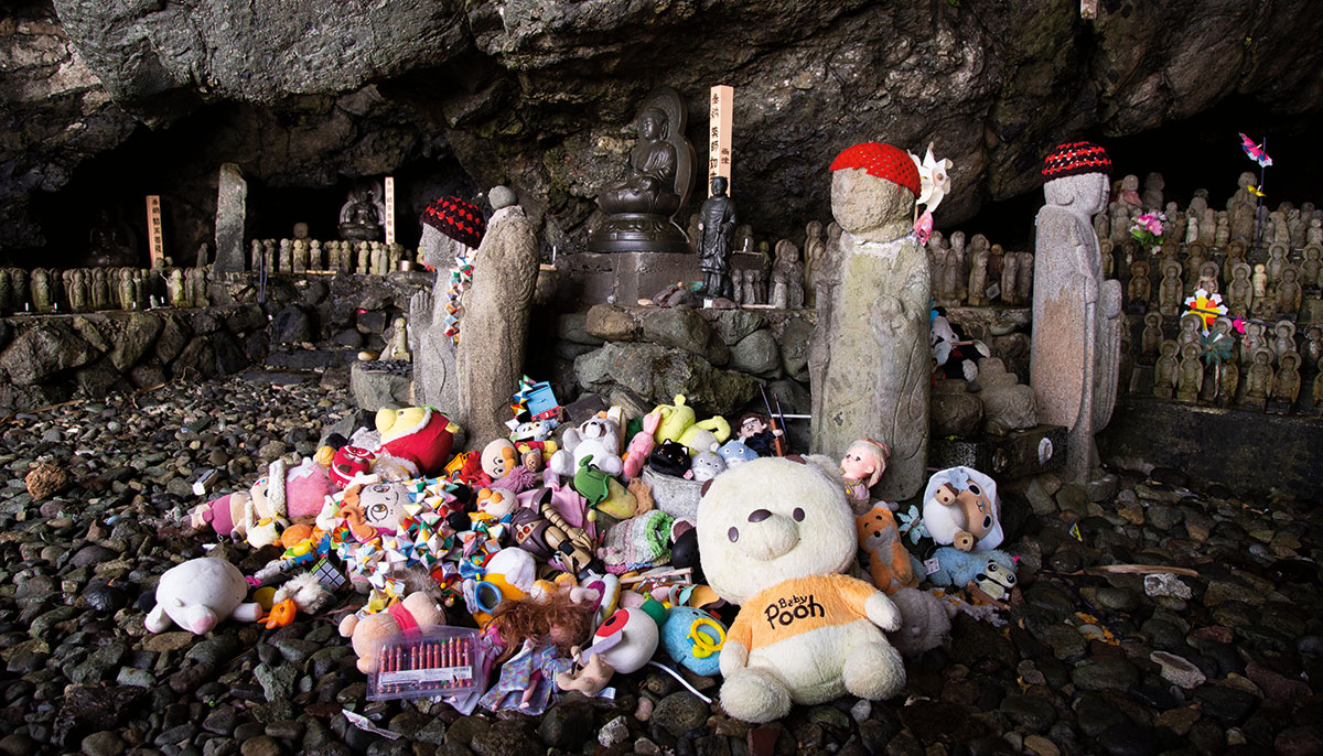 A picture of a bunch of toys in a pile inside of a cave. There are statues wearing red hats near the pile.