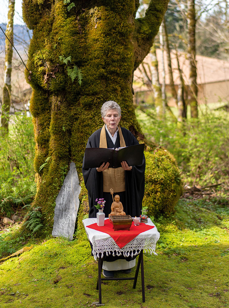 A woman holding a binder in front of an old tree. There is a table in front of her.