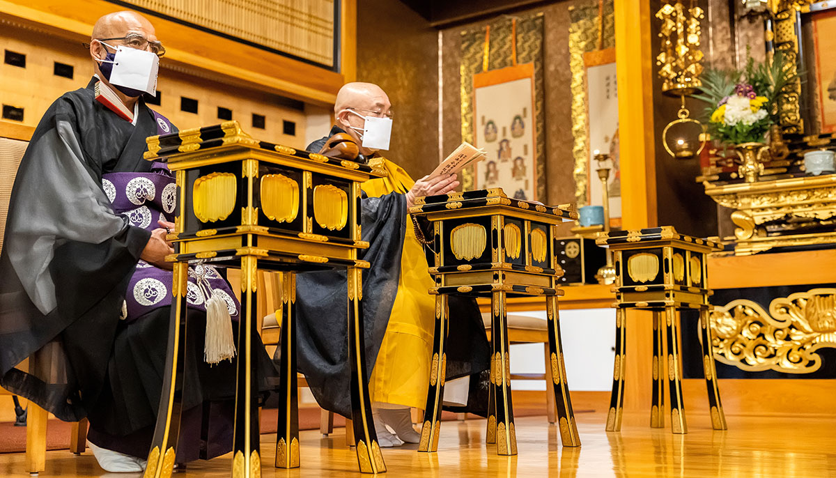 Two men in robes sitting in a gold room with masks on.