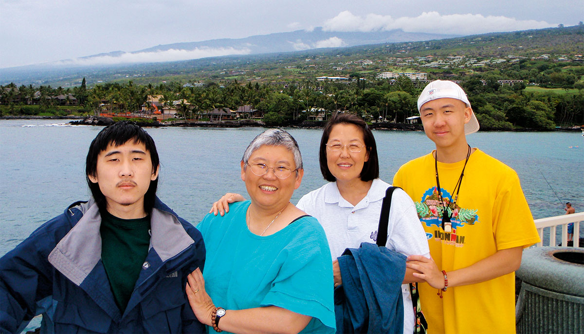 Mushim Ikeda and Rev. Mary Beth Jiko Nakadestand with their sons on a pier with water and trees in the background.