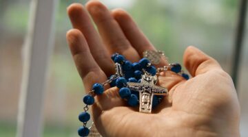 A hand holds a blue Catholic rosary.