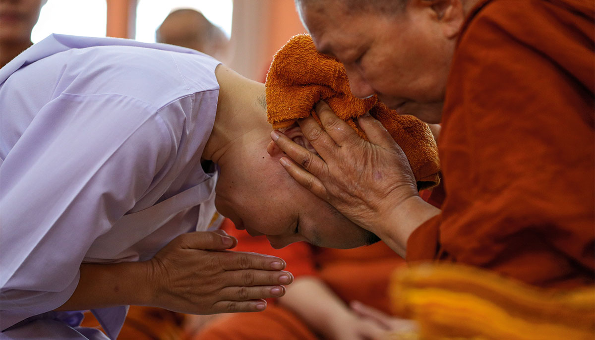 Ven. Dhammananda ordains a nun, covering her head with an orange towel as the nun bows with hands in prayer