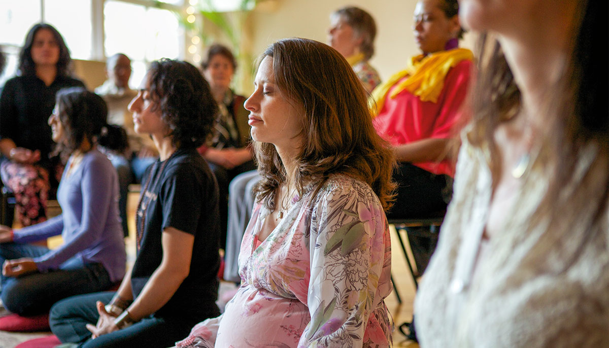 A pregnant woman sits in a group meditation