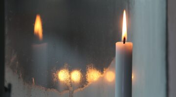 a white candle reflects on a frosted window