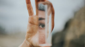 A hand holds a mirror, reflecting an eye looking back at itself.