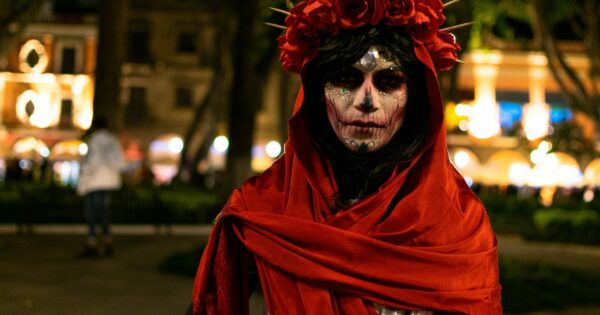 Woman wears crown of red roses and skull face paint.