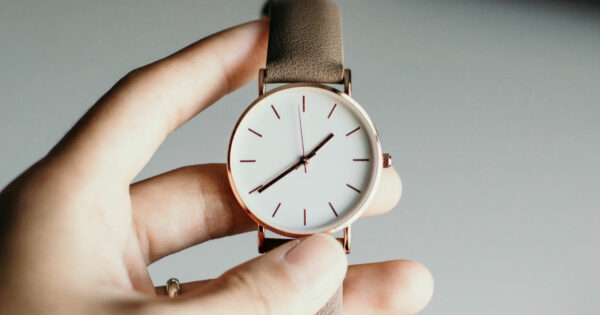 Hand holding a gold wrist watch with a brown leather strap