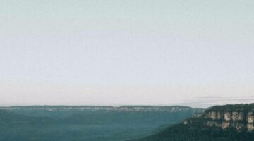 Person sitting on a cliff looking over mountain range.