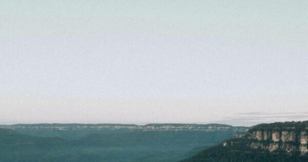 Person sitting on a cliff looking over mountain range.